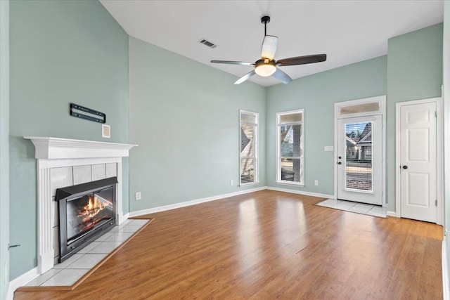 unfurnished living room with visible vents, baseboards, a tile fireplace, wood finished floors, and a ceiling fan