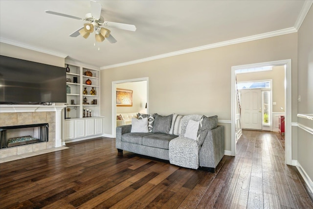 living area with crown molding, baseboards, dark wood-type flooring, a tiled fireplace, and ceiling fan