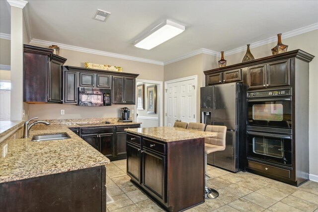 kitchen featuring black appliances, light stone countertops, visible vents, and a sink