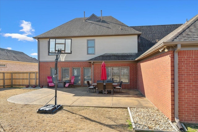 rear view of house with fence, brick siding, roof with shingles, and a patio area