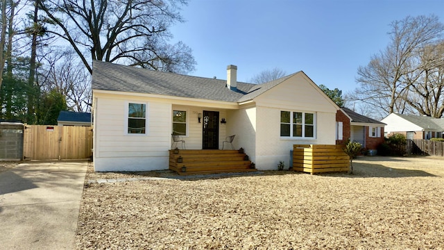 view of front of home with brick siding, a shingled roof, and fence