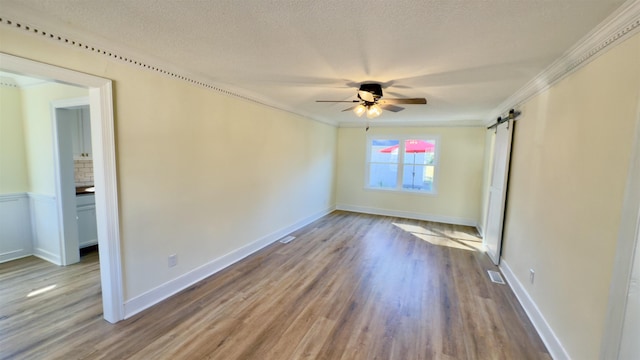 empty room featuring a barn door, wood finished floors, a ceiling fan, and ornamental molding