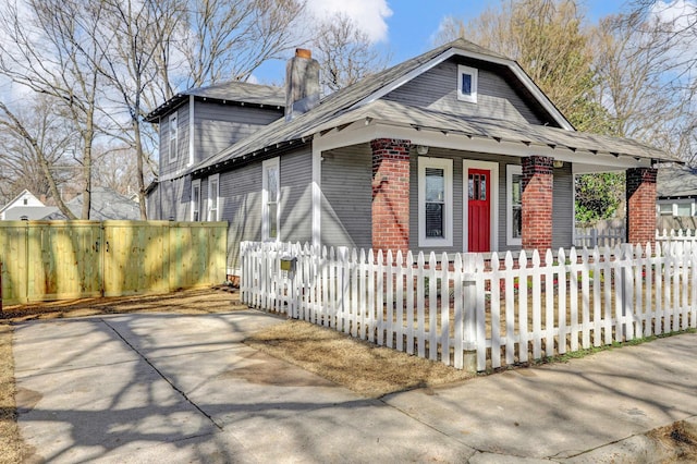 view of front facade featuring a fenced front yard, brick siding, covered porch, and a chimney