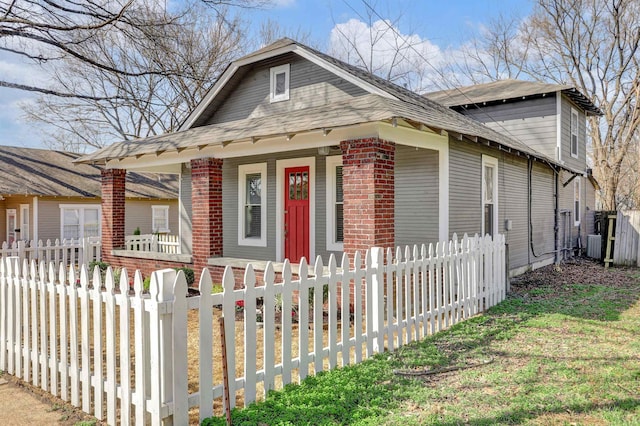 bungalow-style house featuring central air condition unit, brick siding, covered porch, and a fenced front yard