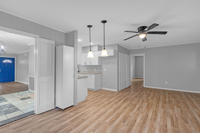 unfurnished living room with ceiling fan with notable chandelier, light wood-style floors, baseboards, and ornamental molding