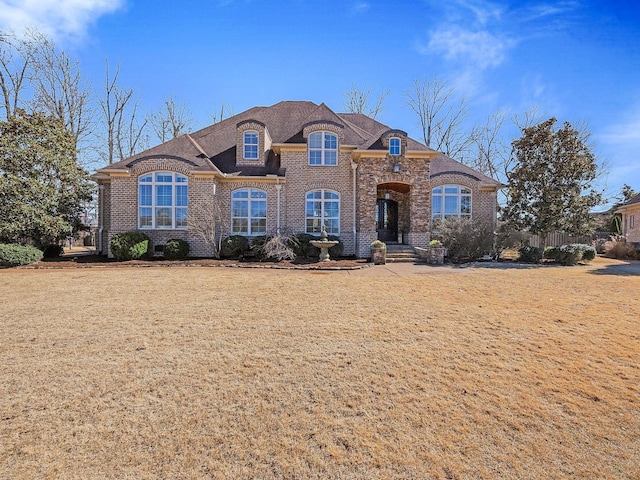 french country style house with brick siding and a front yard