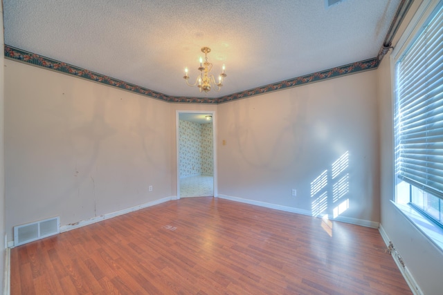 unfurnished room featuring a chandelier, visible vents, a textured ceiling, and wood finished floors