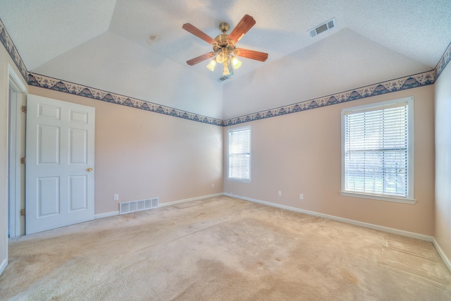 spare room with visible vents, lofted ceiling, and light colored carpet