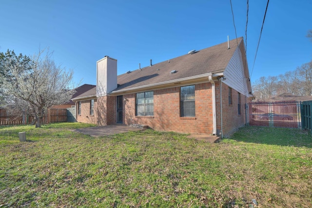 back of house with brick siding, a fenced backyard, a chimney, a patio area, and a lawn