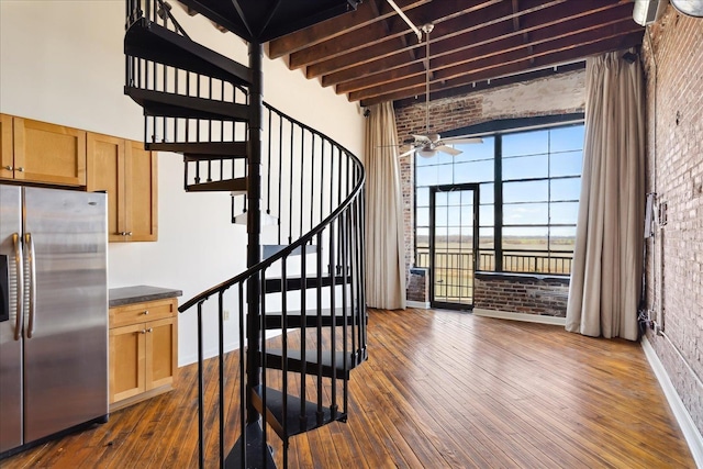 stairway featuring beam ceiling, a high ceiling, wood-type flooring, and brick wall