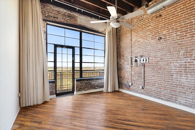 unfurnished room featuring a ceiling fan, baseboards, brick wall, a high ceiling, and hardwood / wood-style flooring