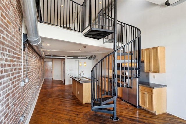 stairs with a high ceiling, wood finished floors, and brick wall