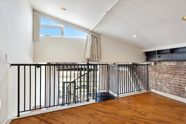 hall featuring wood finished floors, baseboards, brick wall, recessed lighting, and vaulted ceiling