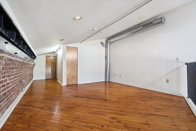 below grade area with baseboards, wood-type flooring, and brick wall