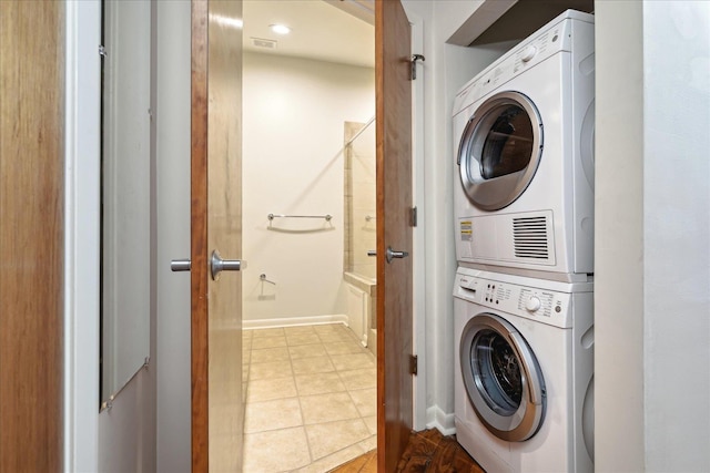 laundry room featuring tile patterned floors, laundry area, stacked washing maching and dryer, and baseboards