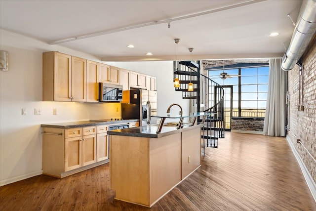 kitchen with light brown cabinets, a sink, dark countertops, stainless steel appliances, and brick wall