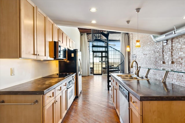 kitchen with brick wall, light wood-style flooring, a sink, stainless steel appliances, and dark countertops