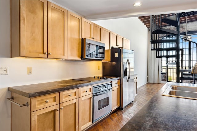 kitchen featuring dark countertops, a sink, light brown cabinets, appliances with stainless steel finishes, and dark wood-style flooring