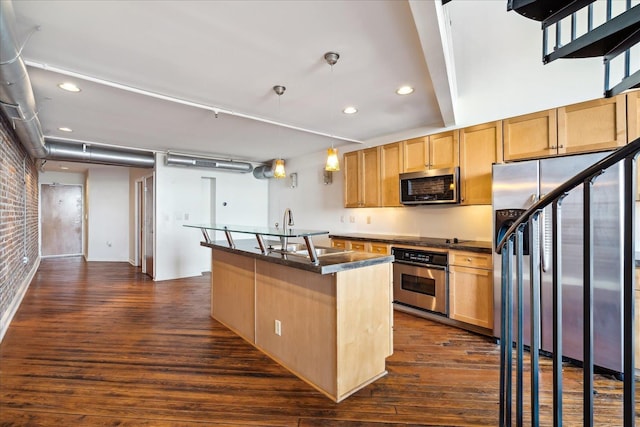 kitchen featuring a center island with sink, brick wall, dark wood-style flooring, appliances with stainless steel finishes, and dark countertops