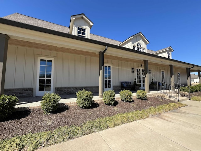 view of front of house featuring a porch, brick siding, board and batten siding, and roof with shingles