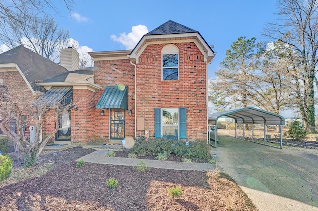 view of front of property with a detached carport, a front lawn, brick siding, and a chimney