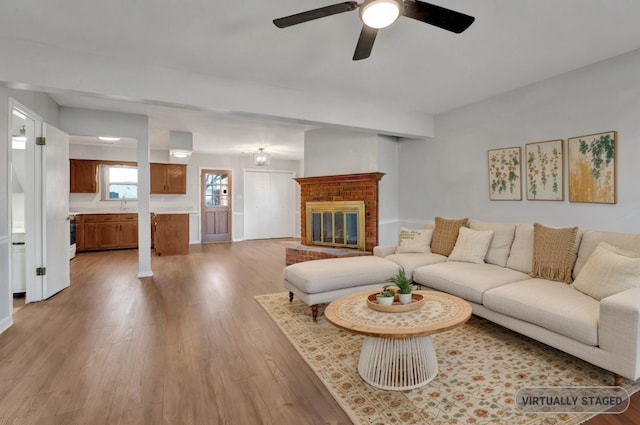 living area with a brick fireplace, wood finished floors, and ceiling fan