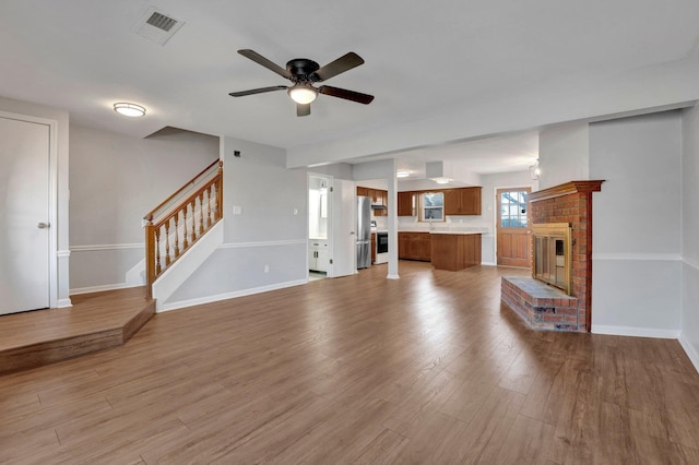 unfurnished living room with stairway, visible vents, baseboards, light wood-style flooring, and a fireplace