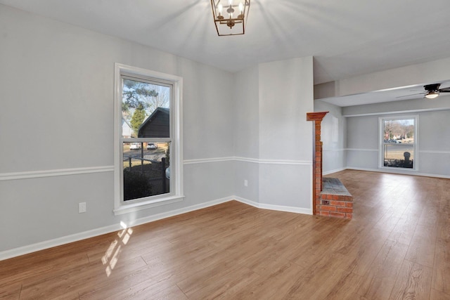 spare room featuring ceiling fan with notable chandelier, wood finished floors, and baseboards