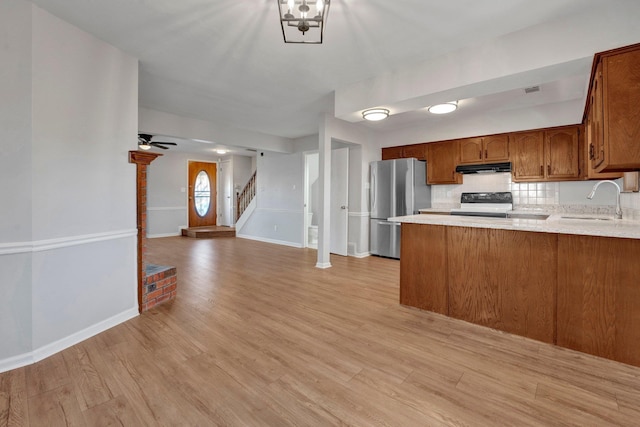 kitchen with under cabinet range hood, freestanding refrigerator, light wood-style floors, electric stove, and a sink