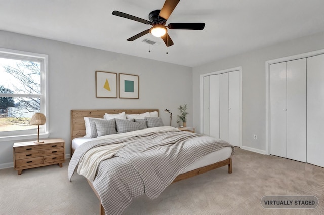 bedroom featuring visible vents, light carpet, two closets, baseboards, and ceiling fan