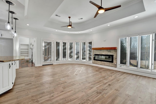 unfurnished living room with a tray ceiling, light wood-style flooring, visible vents, and ceiling fan