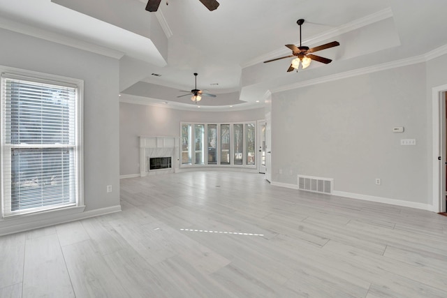 unfurnished living room with baseboards, visible vents, a premium fireplace, crown molding, and a raised ceiling