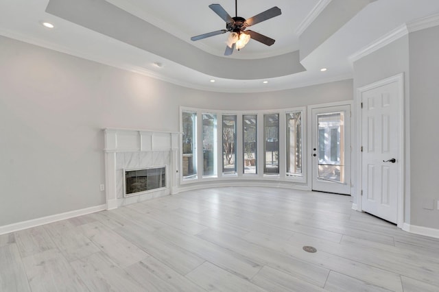 unfurnished living room with light wood-type flooring, a tray ceiling, baseboards, and a high end fireplace