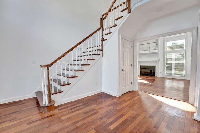 stairs featuring baseboards, wood-type flooring, a high ceiling, and a fireplace