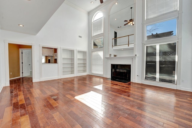 unfurnished living room with a ceiling fan, baseboards, a fireplace with flush hearth, wood-type flooring, and crown molding