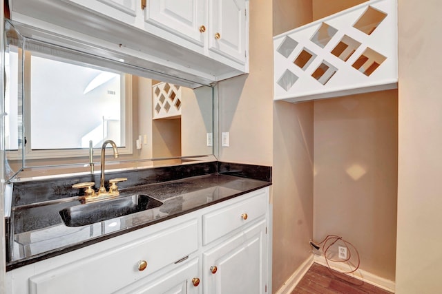 kitchen with wood finished floors, baseboards, a sink, white cabinets, and dark countertops