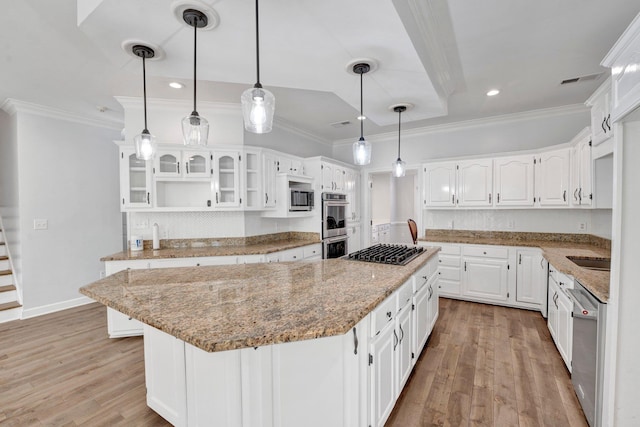 kitchen with light stone counters, light wood finished floors, a kitchen island, appliances with stainless steel finishes, and crown molding