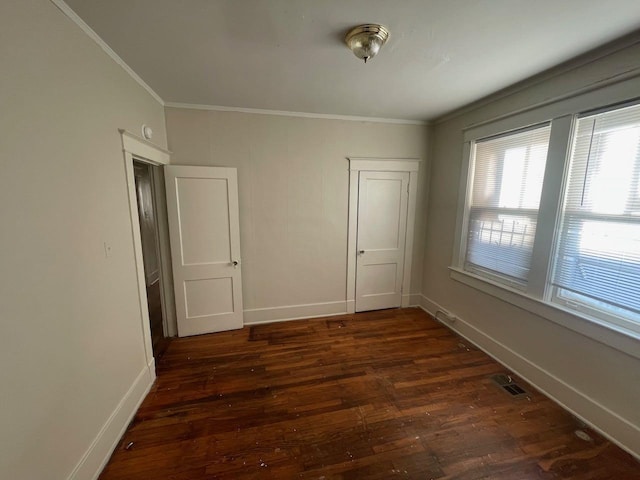 spare room featuring dark wood-style floors, visible vents, crown molding, and baseboards