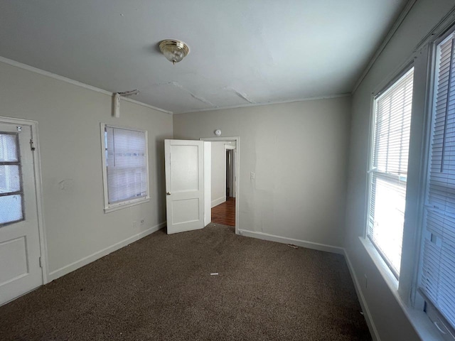 empty room featuring crown molding, baseboards, and dark colored carpet