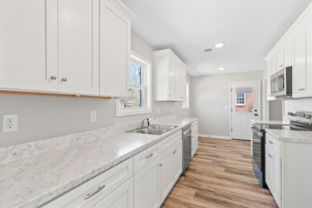 kitchen with visible vents, a sink, appliances with stainless steel finishes, white cabinets, and light wood finished floors