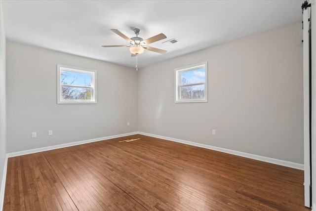 unfurnished room with hardwood / wood-style floors, a healthy amount of sunlight, visible vents, and baseboards