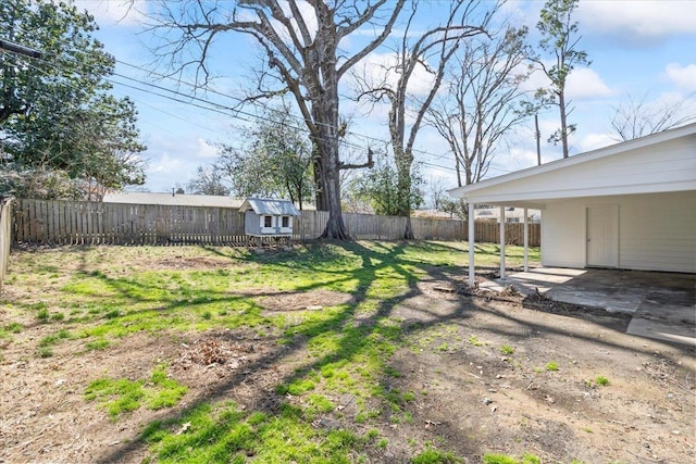 view of yard with a patio, driveway, a fenced backyard, an outdoor structure, and a carport