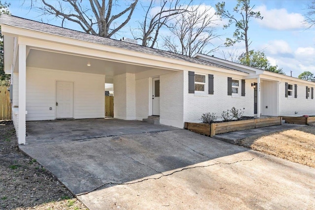 ranch-style house featuring entry steps, concrete driveway, a shingled roof, an attached carport, and brick siding