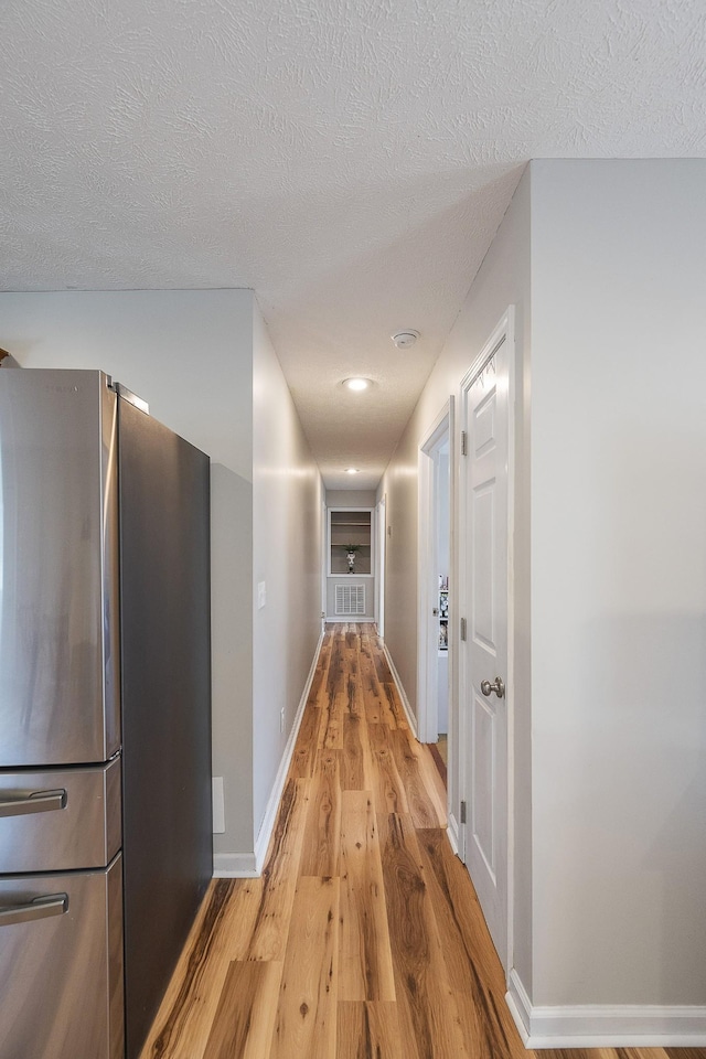 corridor with a textured ceiling, baseboards, and light wood-style floors