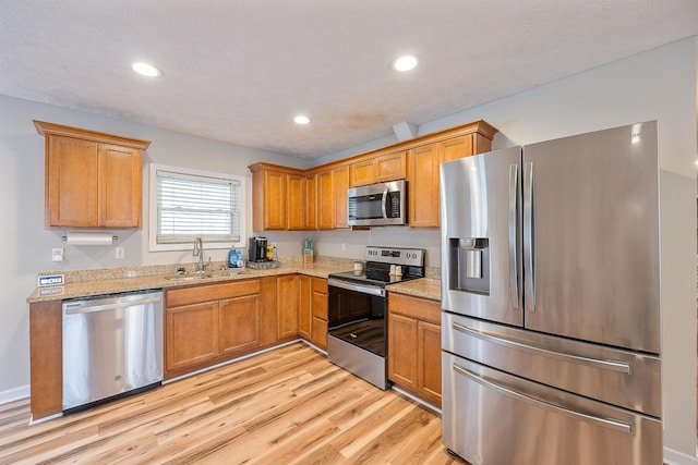 kitchen featuring light stone counters, light wood-style floors, appliances with stainless steel finishes, and a sink