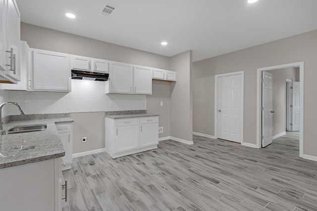 kitchen featuring a sink, under cabinet range hood, white cabinets, light wood finished floors, and light stone countertops