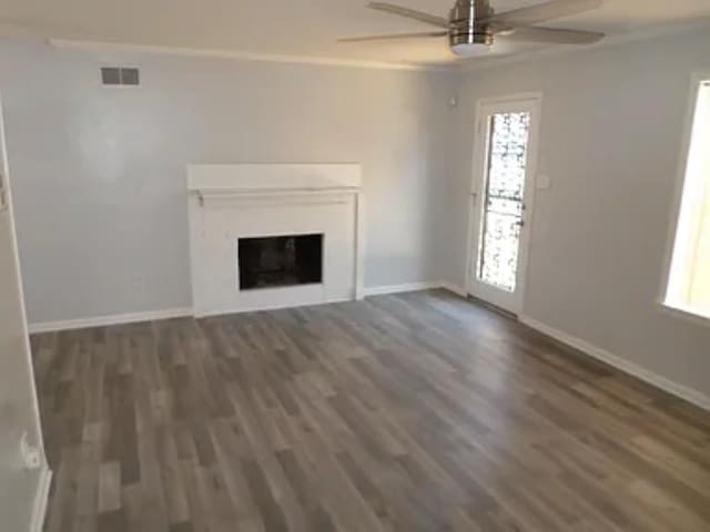 unfurnished living room featuring wood finished floors, visible vents, a fireplace, ceiling fan, and crown molding