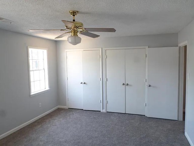 unfurnished bedroom featuring carpet flooring, a textured ceiling, two closets, and visible vents