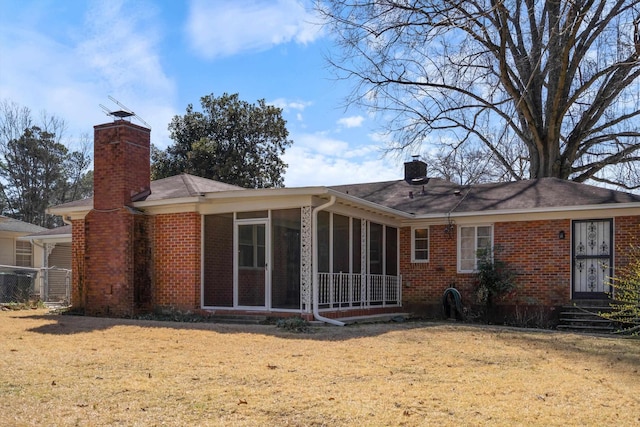 rear view of property with entry steps, a yard, a sunroom, brick siding, and a chimney