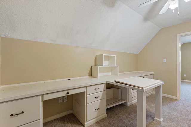 unfurnished office with light carpet, a ceiling fan, built in desk, and vaulted ceiling